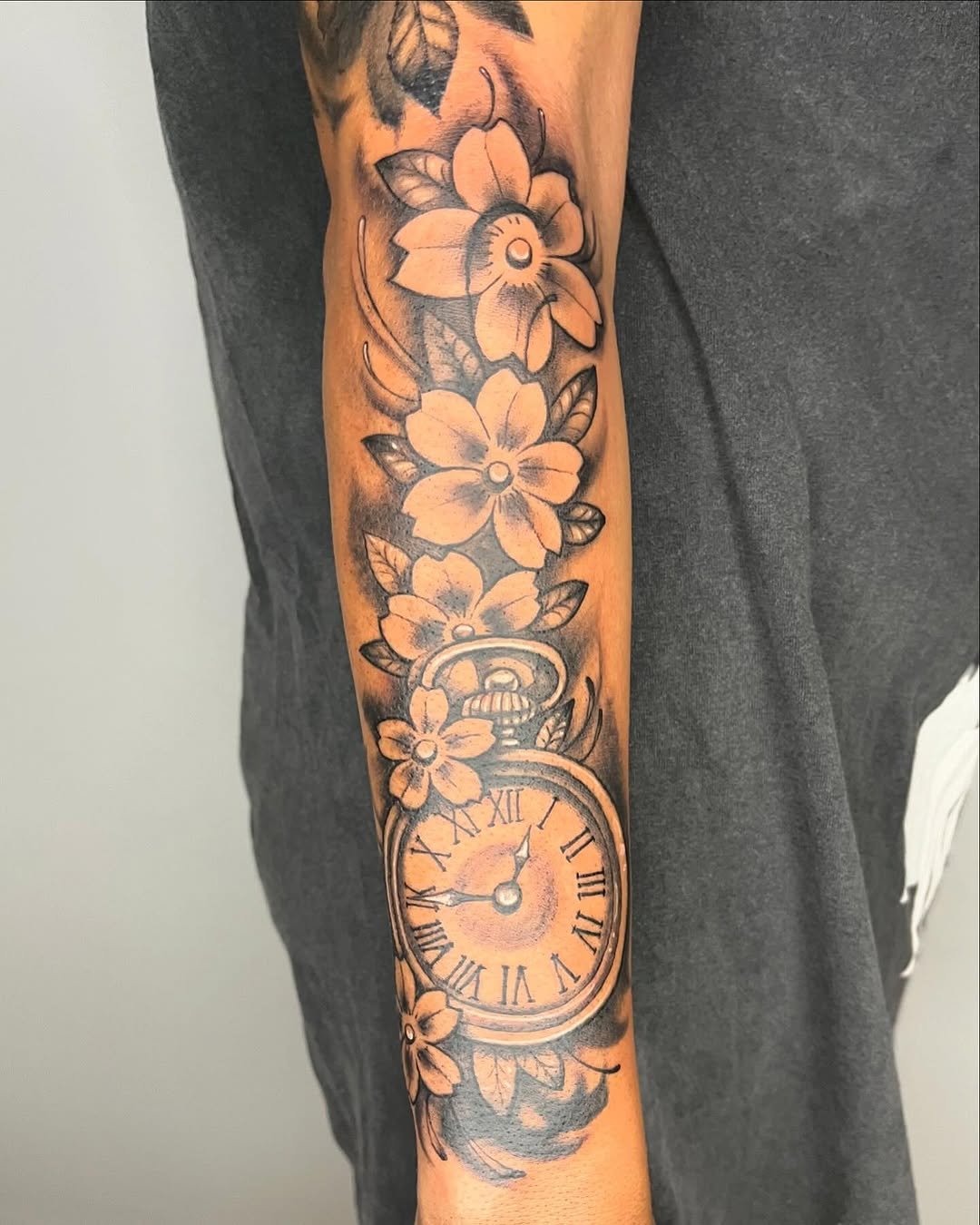 Tatuaje profesional en estudio MartinK Tattoo de un reloj entre flores