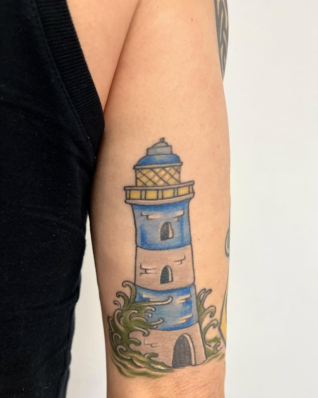 Tatuaje profesional en estudio MartinK Tattoo de un faro rodeado de olas