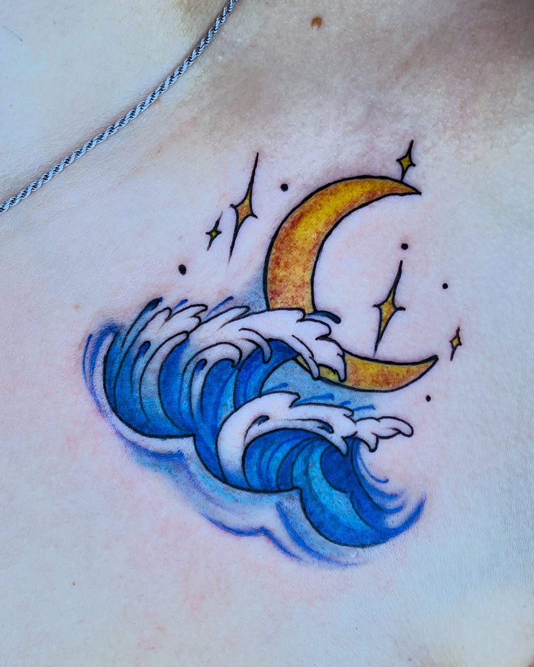 Tatuaje artístico profesional en estudio MartinK Tattoo de una luna creciente sobre las olas del mar